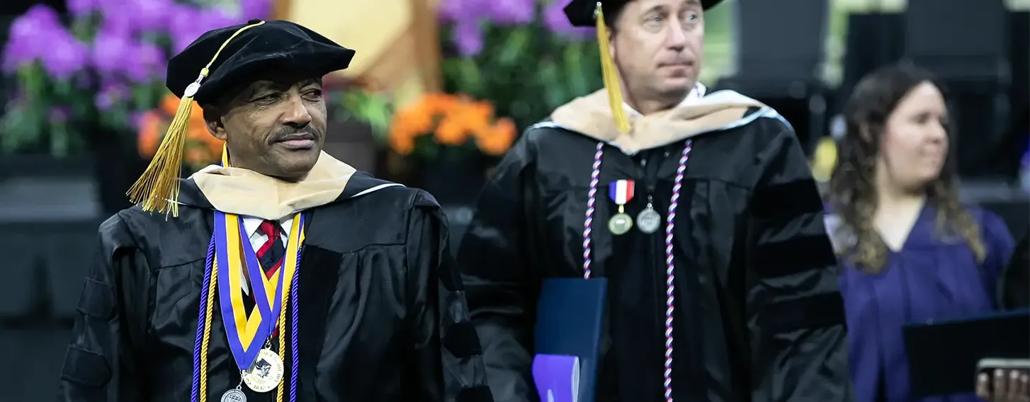 Two men in graduation robes walking down a stage.